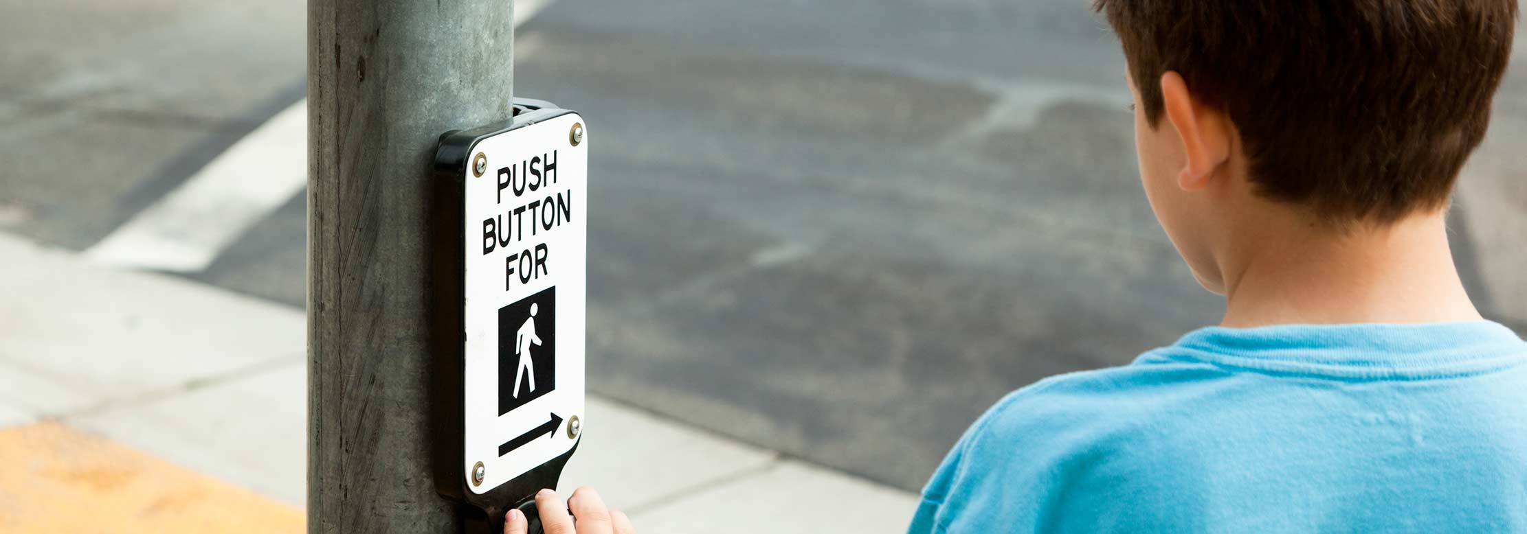 Young person pushes button to activate crosswalk light.