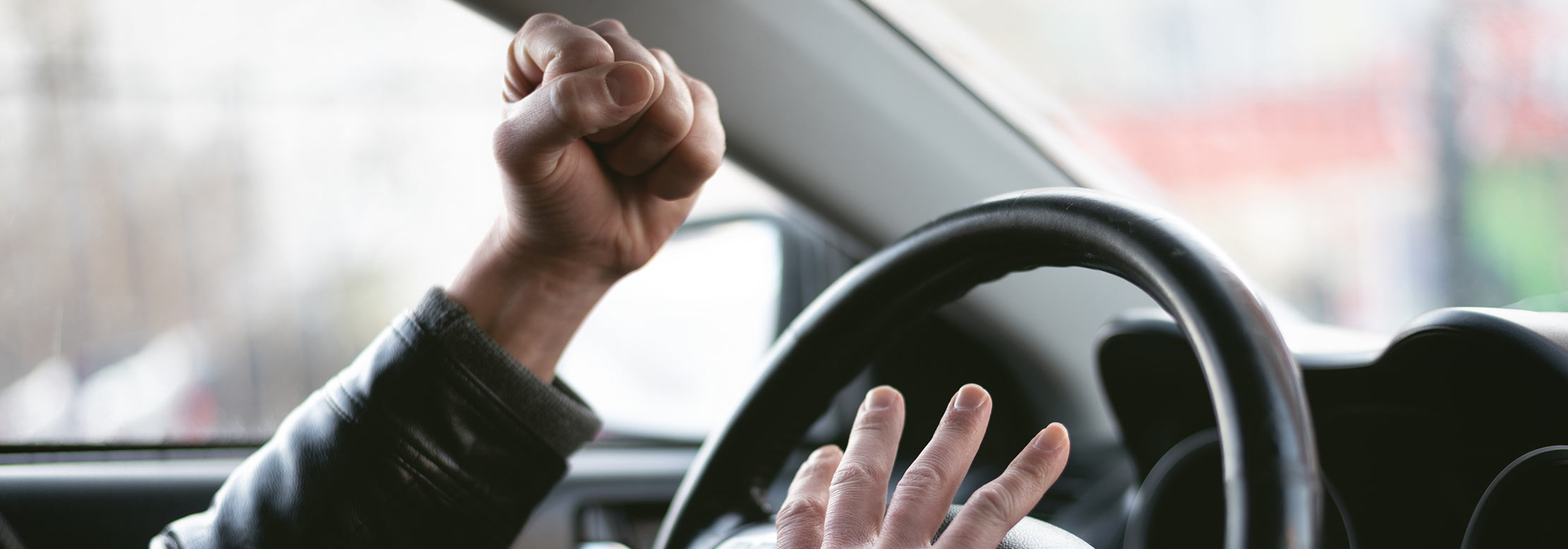 Aggressive driver pumps fist with anger behind the wheel. 