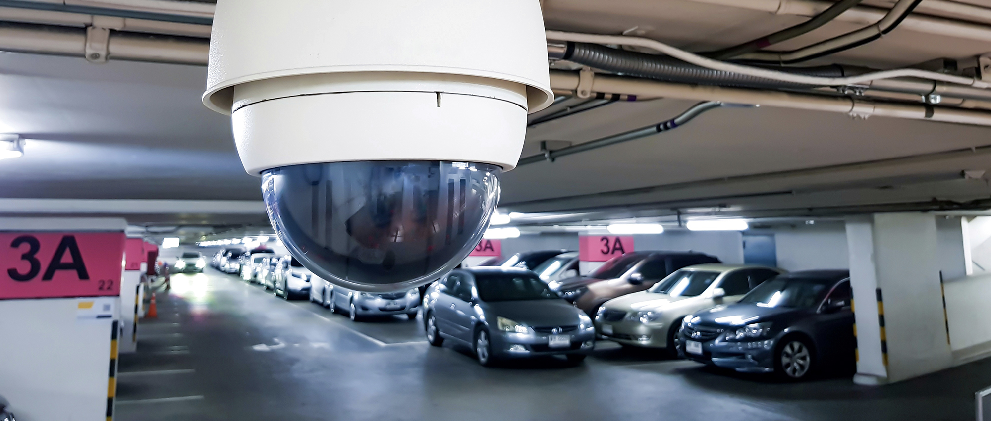 Security camera hovers underground parking lot.