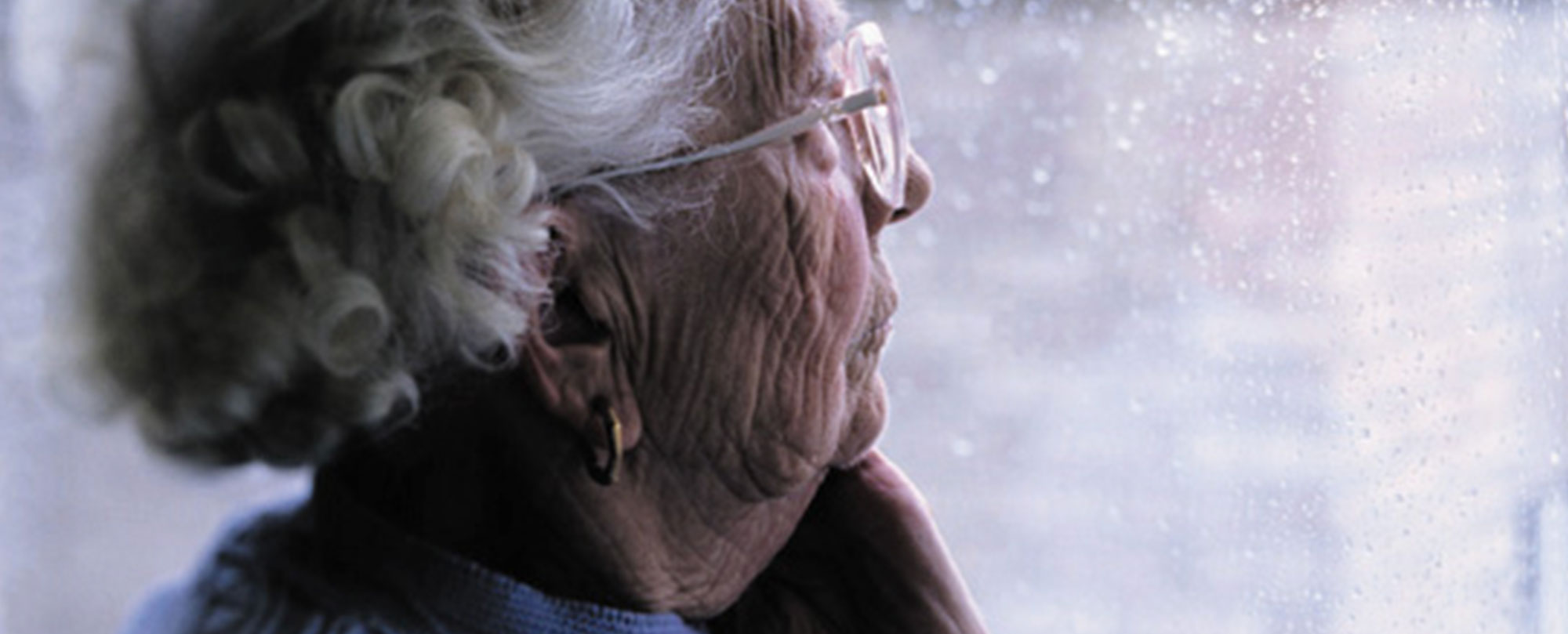 Elderly woman looking through window worried about nursing home care