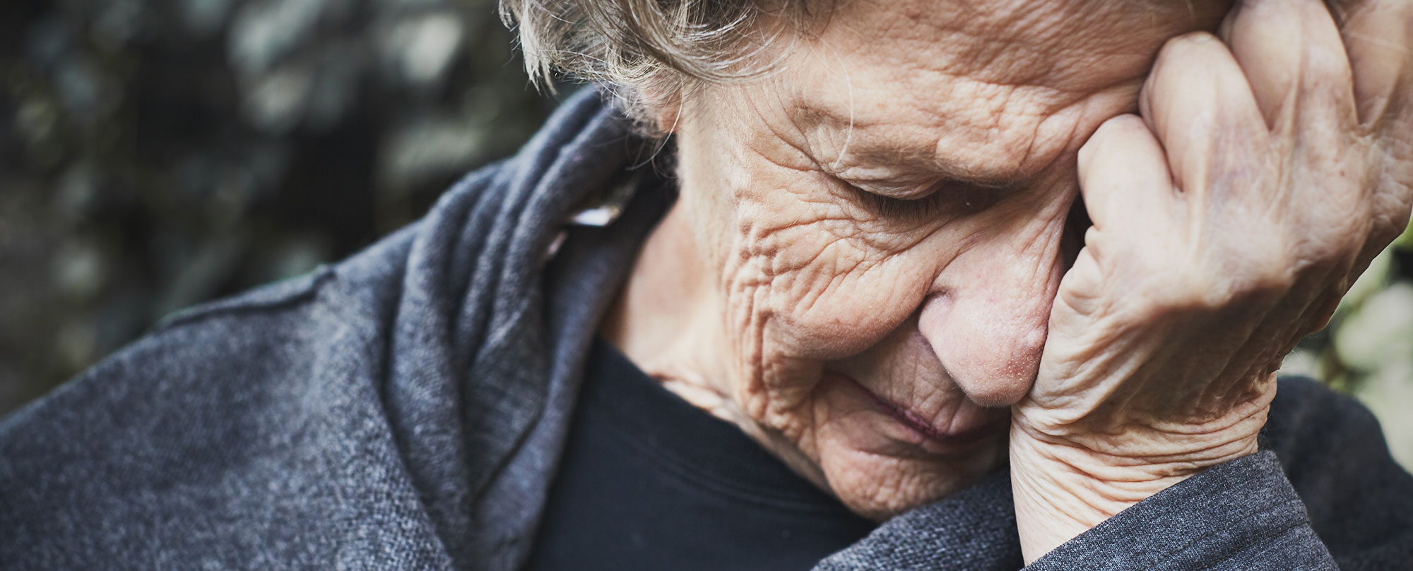 elderly woman with her face in her hands experiencing emotional discomfort