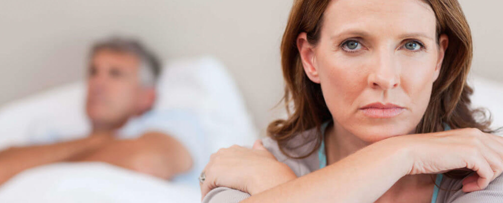 adult woman looking concerned with faded image of older man in bed