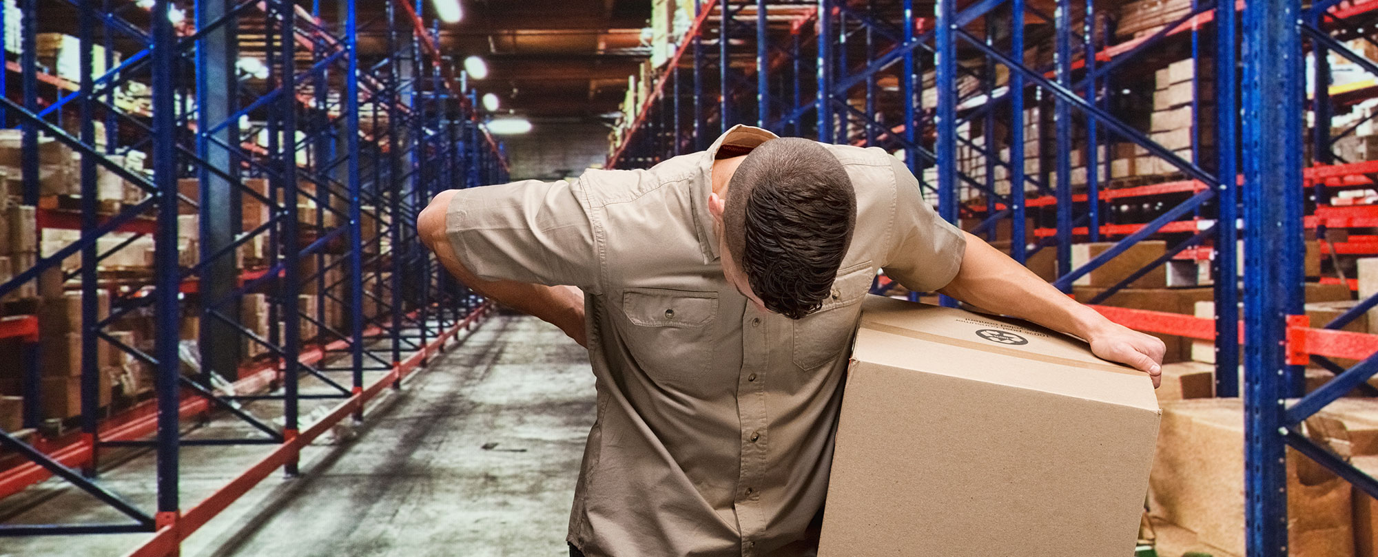 man carrying a box through a warehouse and holding his back in pain