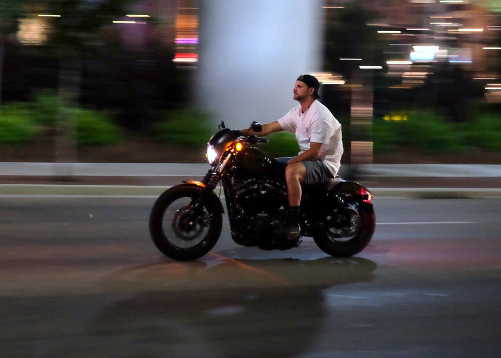 A man is riding a motorcycle at night with city lights in the background.