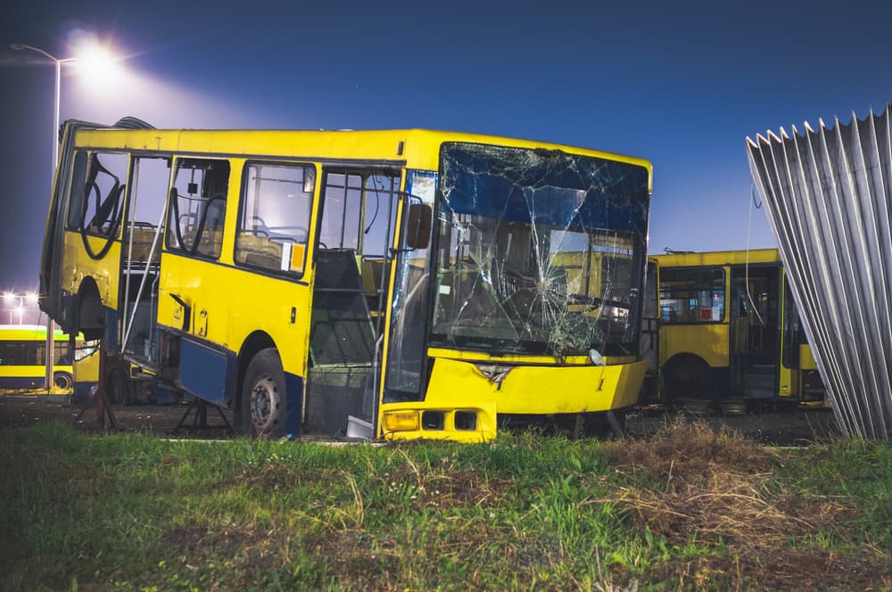 Damaged public transportation bus, remnants after a car accident, at a spare parts yard during the night.