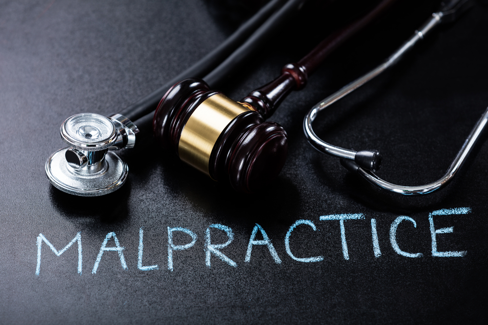 A Conceptual Representation of Medical Malpractice Featuring a Judge's Gavel and a Stethoscope on a Dark Chalkboard Background.