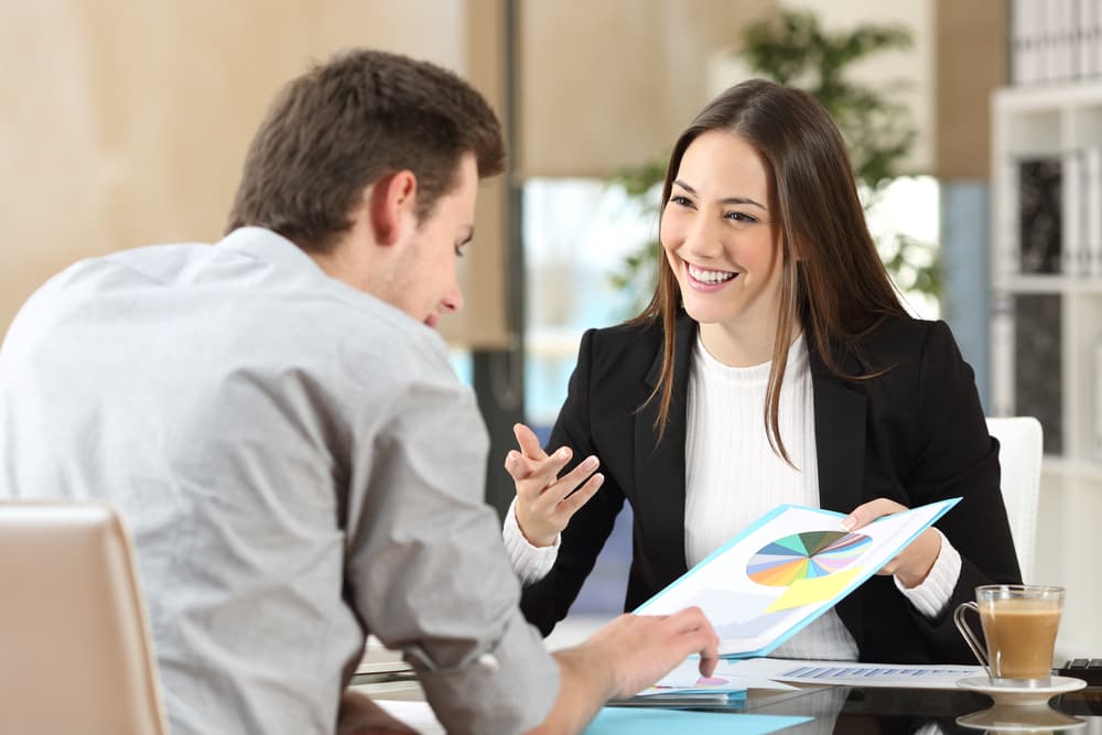 Smiling business people in a coworking space discussing growth graphics, engaging in a productive office conversation.