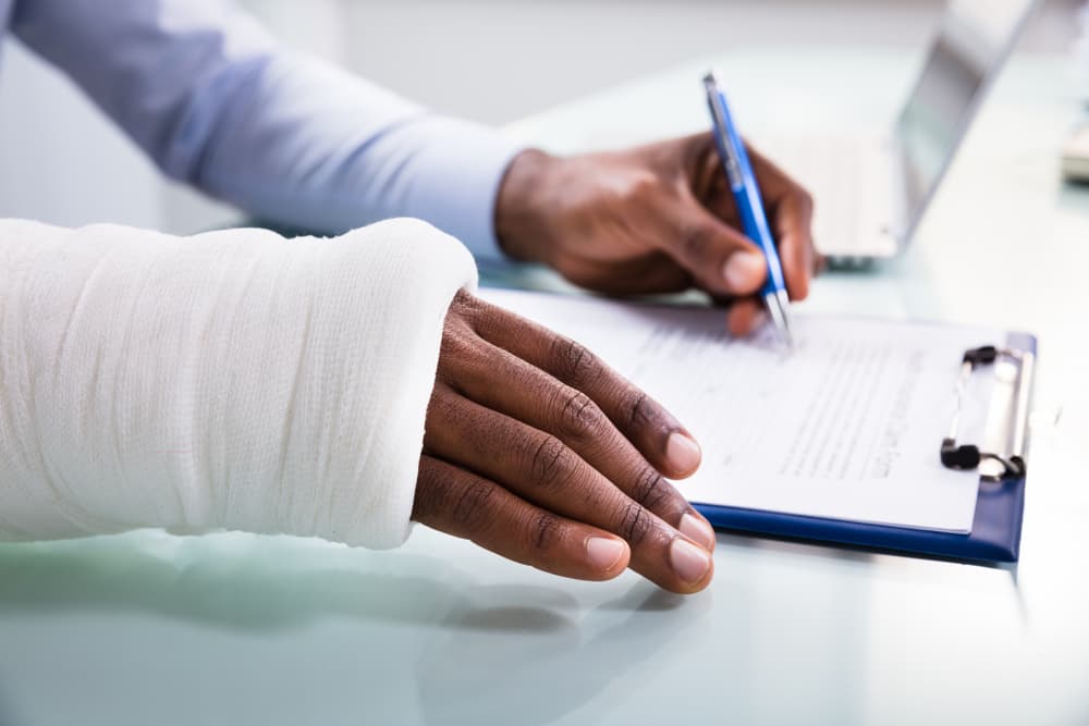 Person with a bandaged arm signing documents, possibly related to taking legal action for a motorcycle accident claim