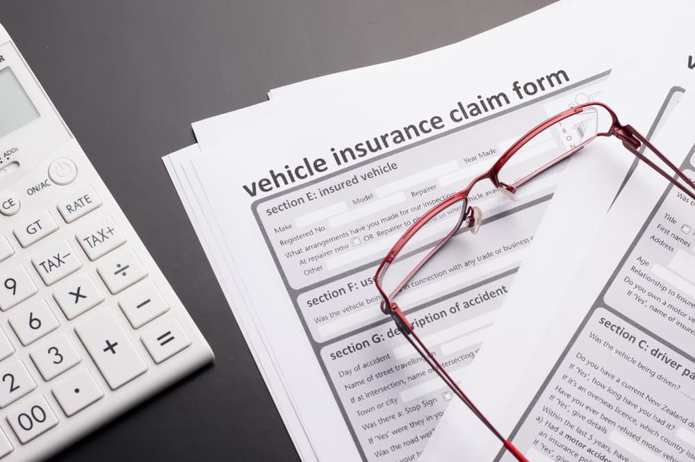 Vehicle insurance claim forms with sections for details, a calculator, and glasses resting on top, on a dark surface.