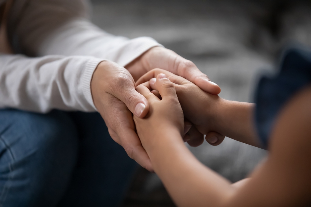 Close up of a caring foster parent holding a child's hands, offering emotional support at home.