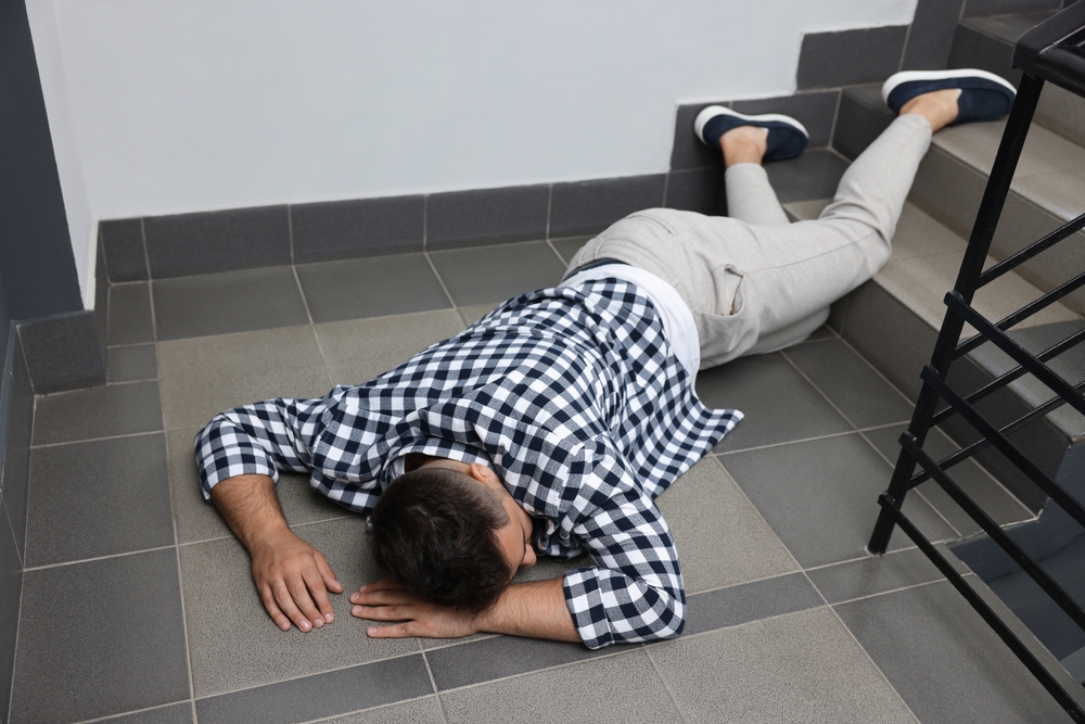 Unconscious man lying on the floor after a fall down the stairs indoors.