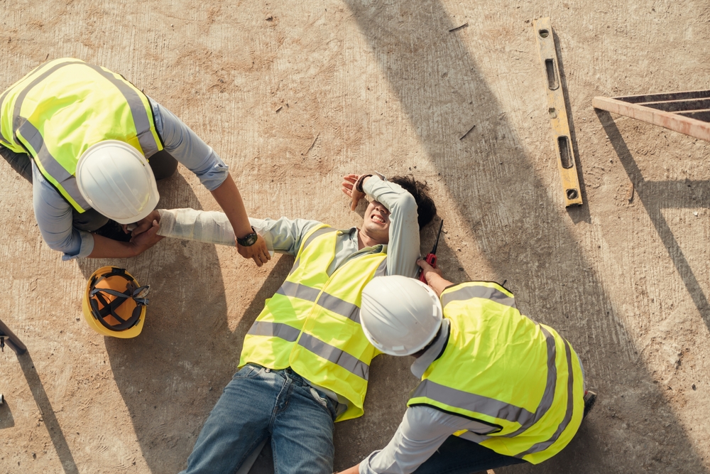 first aid worker treating an arm injury from a construction accident, where a builder fell from scaffolding to the concrete floor. Safety team assisting.