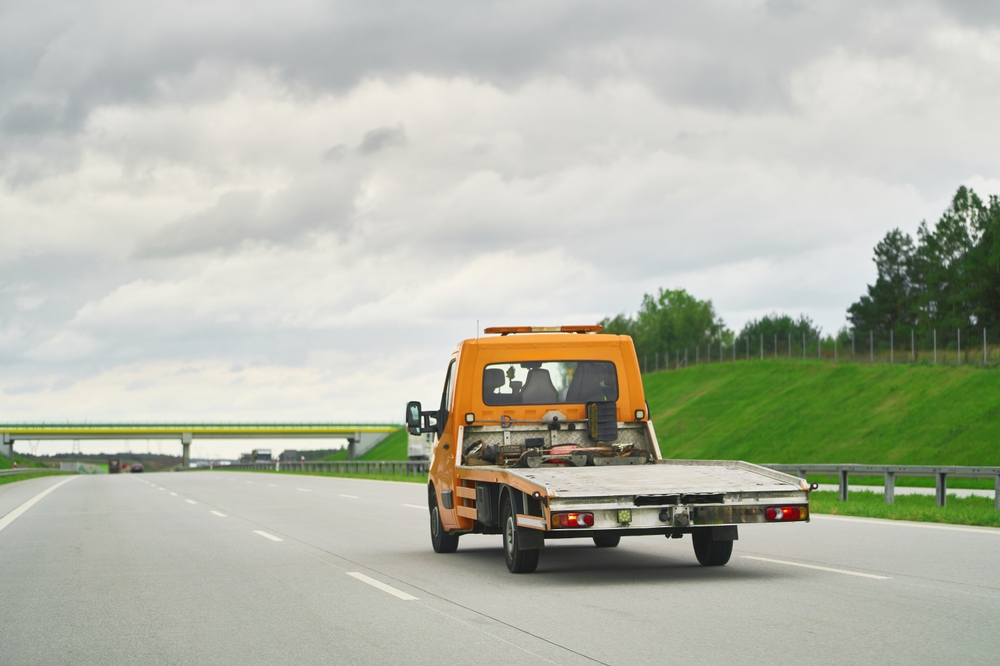 Tow truck transporter on the highway providing roadside assistance. An empty car carrier tow truck driving fast on the road.