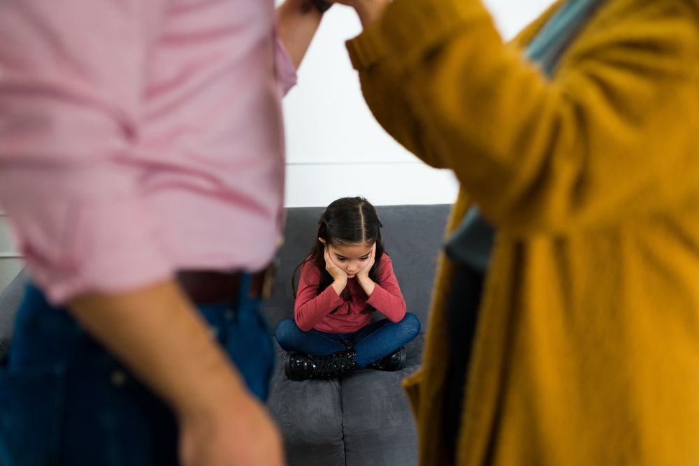 A sad child feeling distressed amid her parents' fight over child custody after divorce.