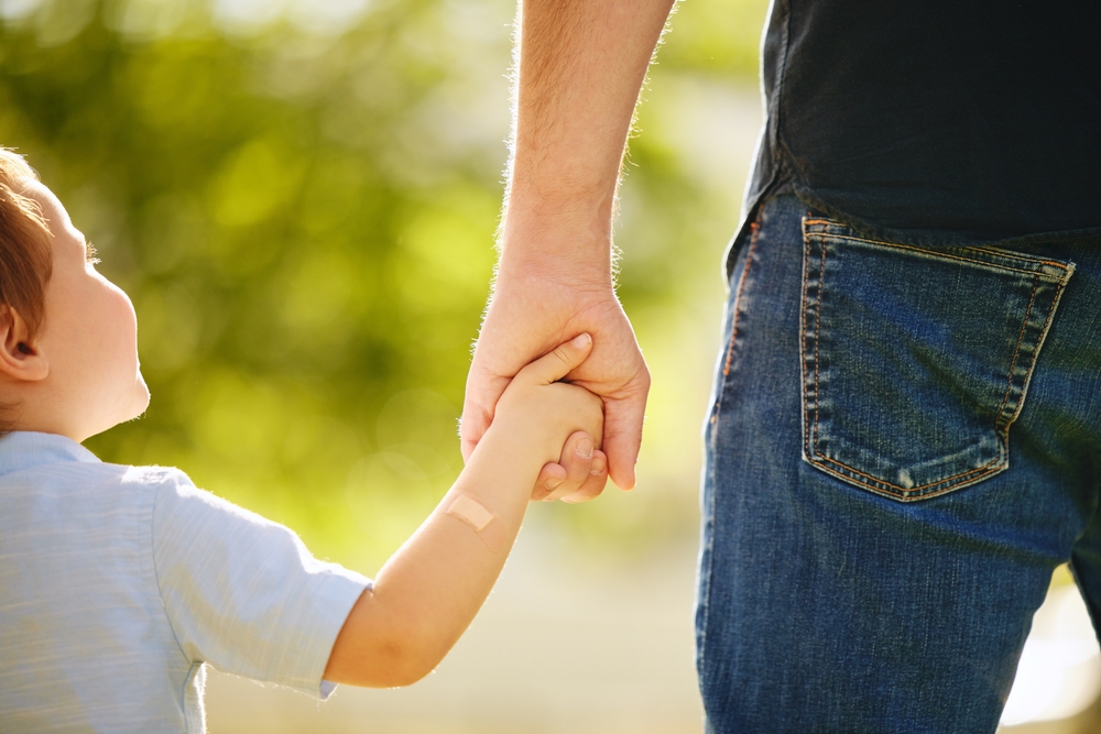 Father and child holding hands in a park, enjoying bonding and trust on a summer vacation.