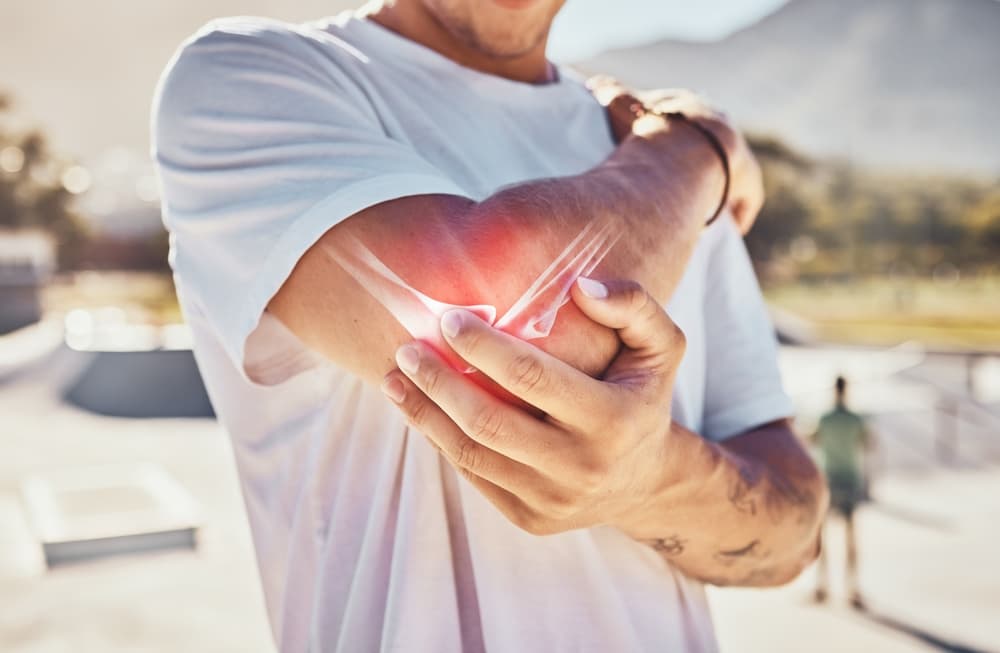 Close-up of a man receiving elbow arthritis massage in a summer urban park, focusing on joint pain and physical therapy.