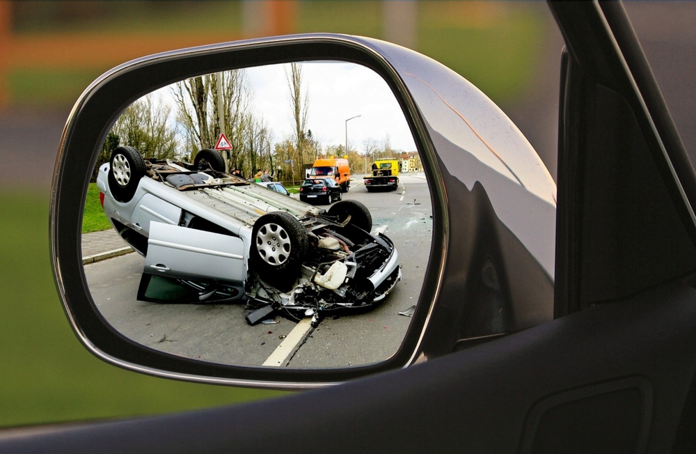 The photo shows a car accident reflected in another vehicle's side mirror, revealing a damaged car amidst scattered debris.