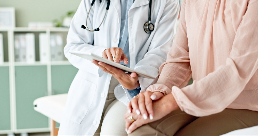 Doctor in a clinic uses a tablet to consult with a patient, emphasizing healthcare, medical expenses, and digital tech in care.