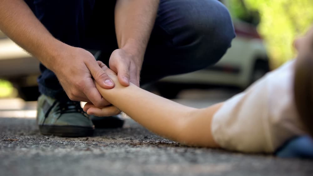 Man holding hand of girl lying on road, unconscious victim of car accident,