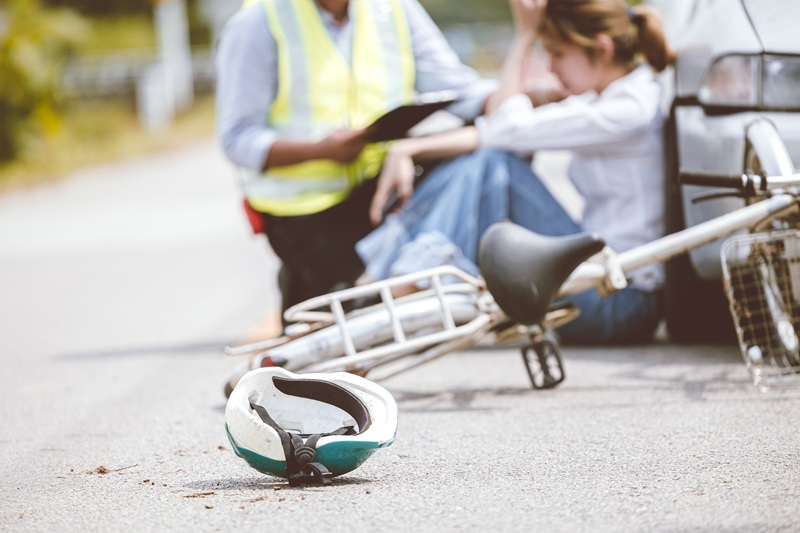 Woman injured in a bicycle accident. She is sitting on the ground while an officer collects evidence