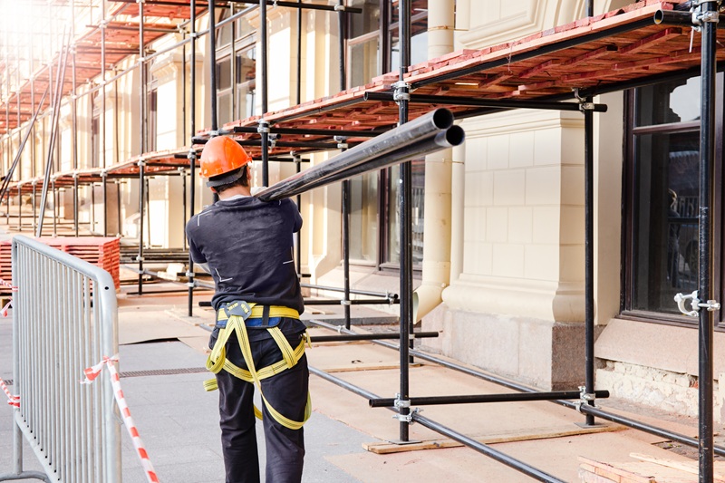 builder carries a steel beam on his shoulder. Construction site, building construction and reconstruction process.