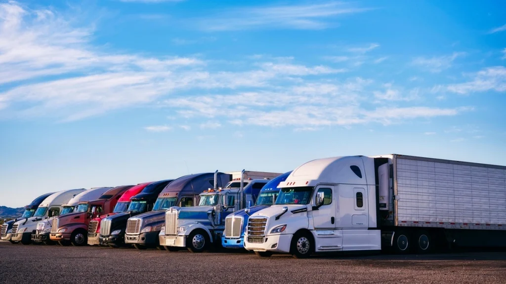 A row of different semi-trucks parked in a gravel lot