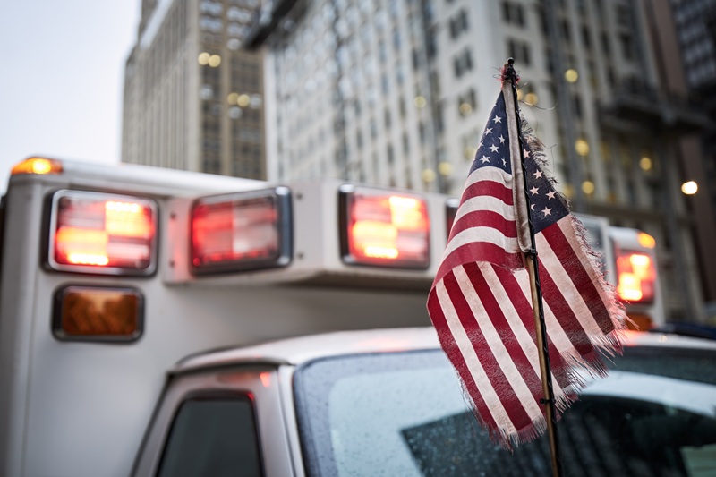 Close-up of American flag against red flasher light of siren of ambulance car.