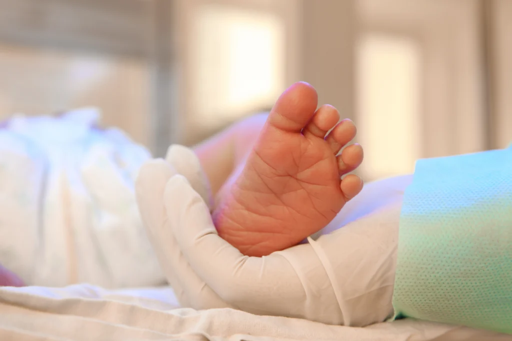 A doctor is cradling a newborn baby's foot in a medical setting.