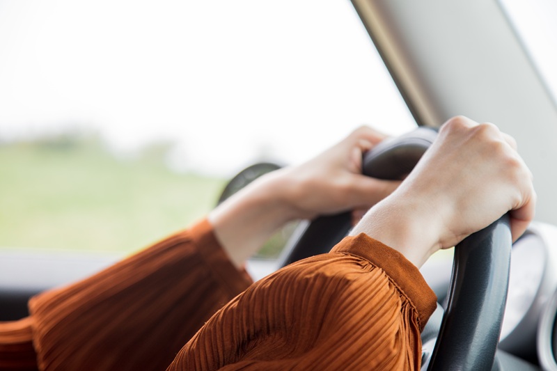 Female holding hands on a steering wheel in a car. Closeup view