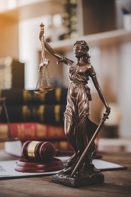 Lady Justice sitting on a desk with a gavel and legal books in the background.