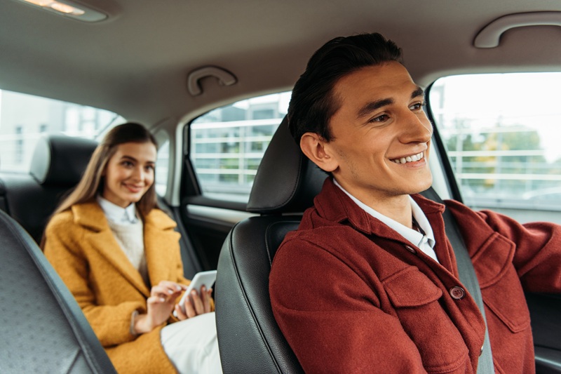 Selective focus of smiling rideshare driver and woman with smartphone in car
