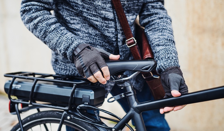 A midsection of an unrecognizable cyclist with electrobike standing outdoors in town.