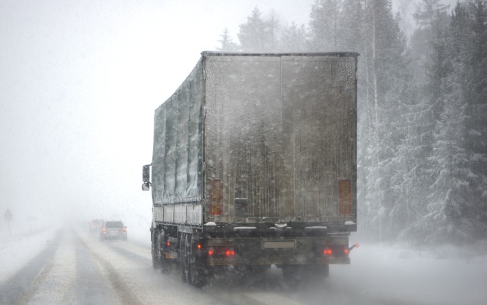 A semi truck is driving through heavy snow and icy conditions.